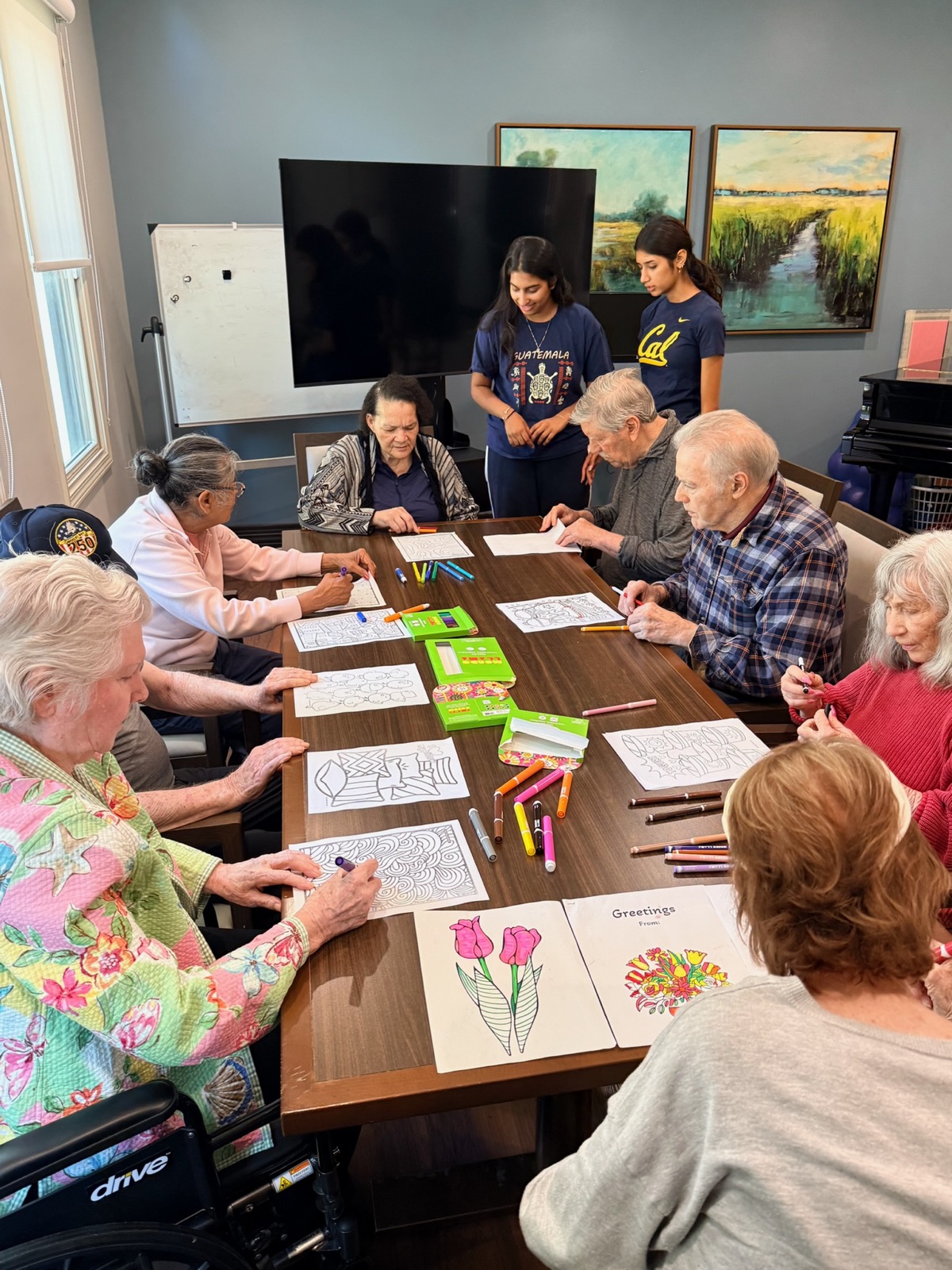 Residents coloring and making greeting cards around a table while two facilitators look on
