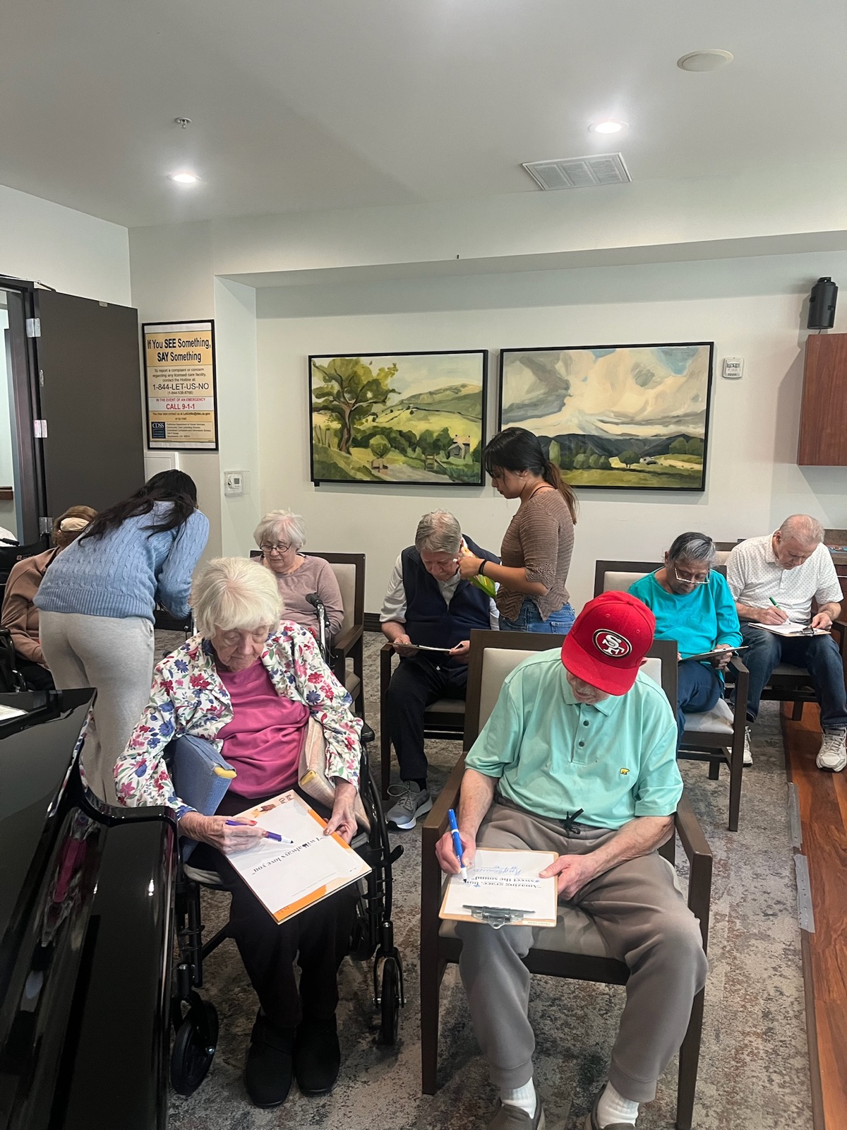 Residents seated in a circle writing on clipboards while a facilitator helps one of them