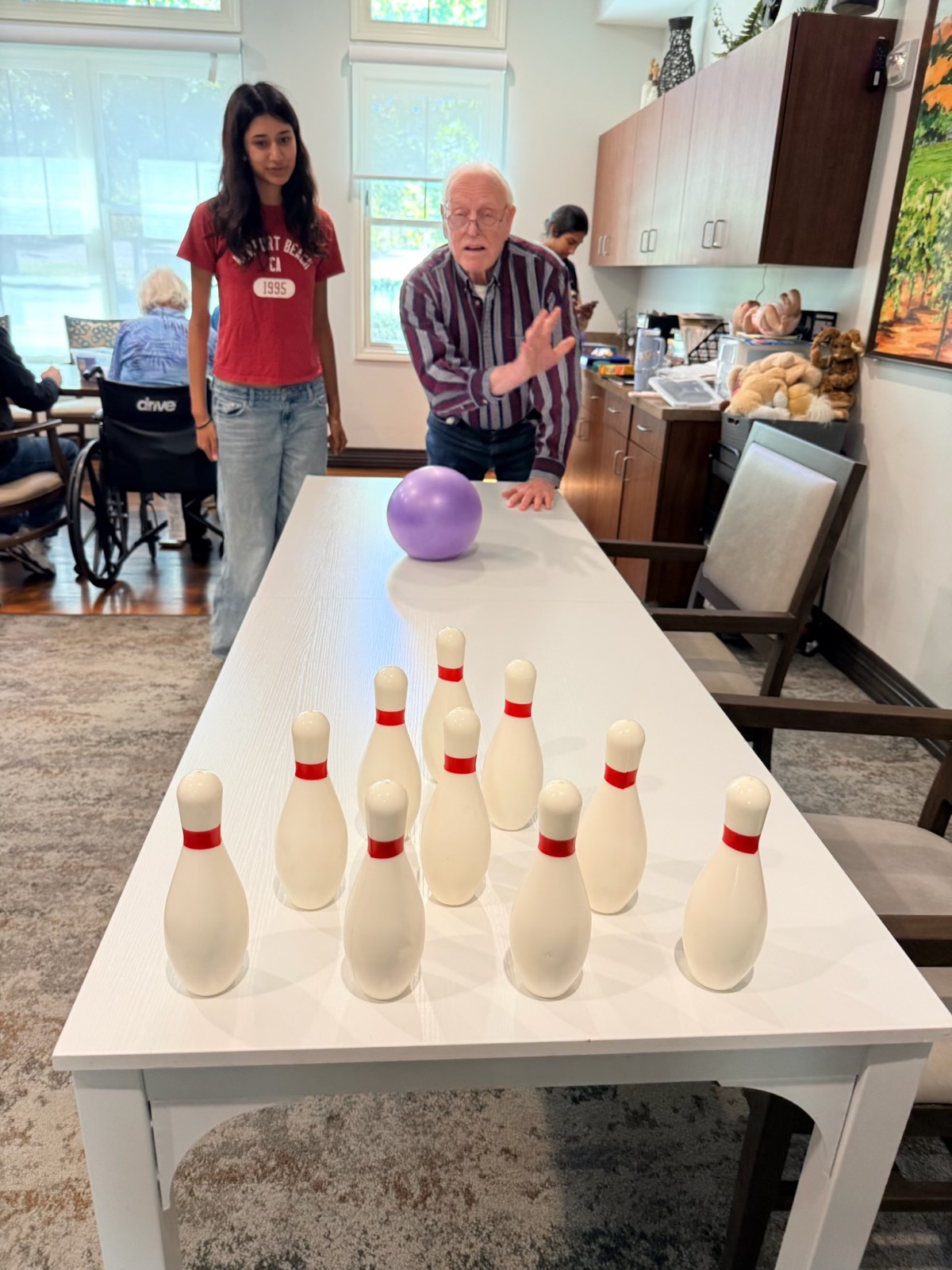 A resident rolling a ball toward tabletop bowling pins as a facilitator watches